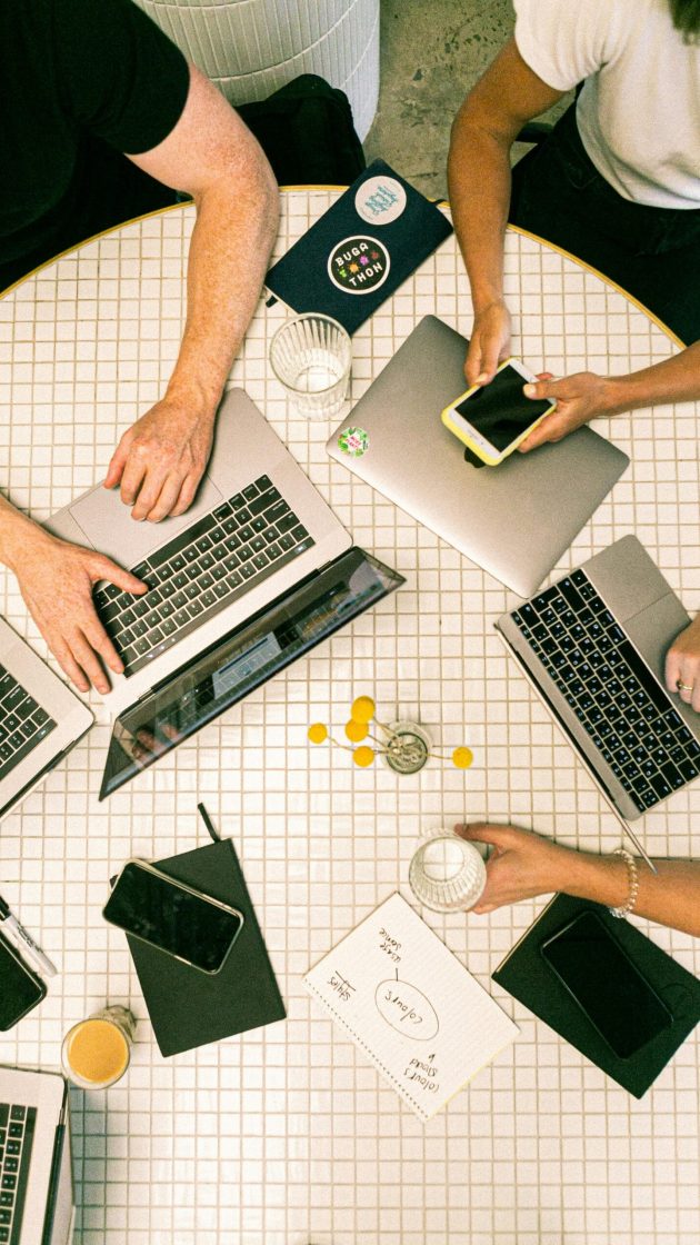 Top view of a team working together on laptops, smartphones, notebooks, and coffee around a tiled table during a collaborative digital project.